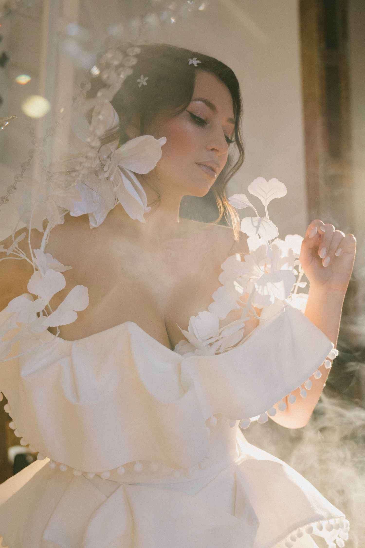 Close portrait of Lilia Mai in white couture, veiled in soft haze with hand-cut paper florals at her shoulder.
